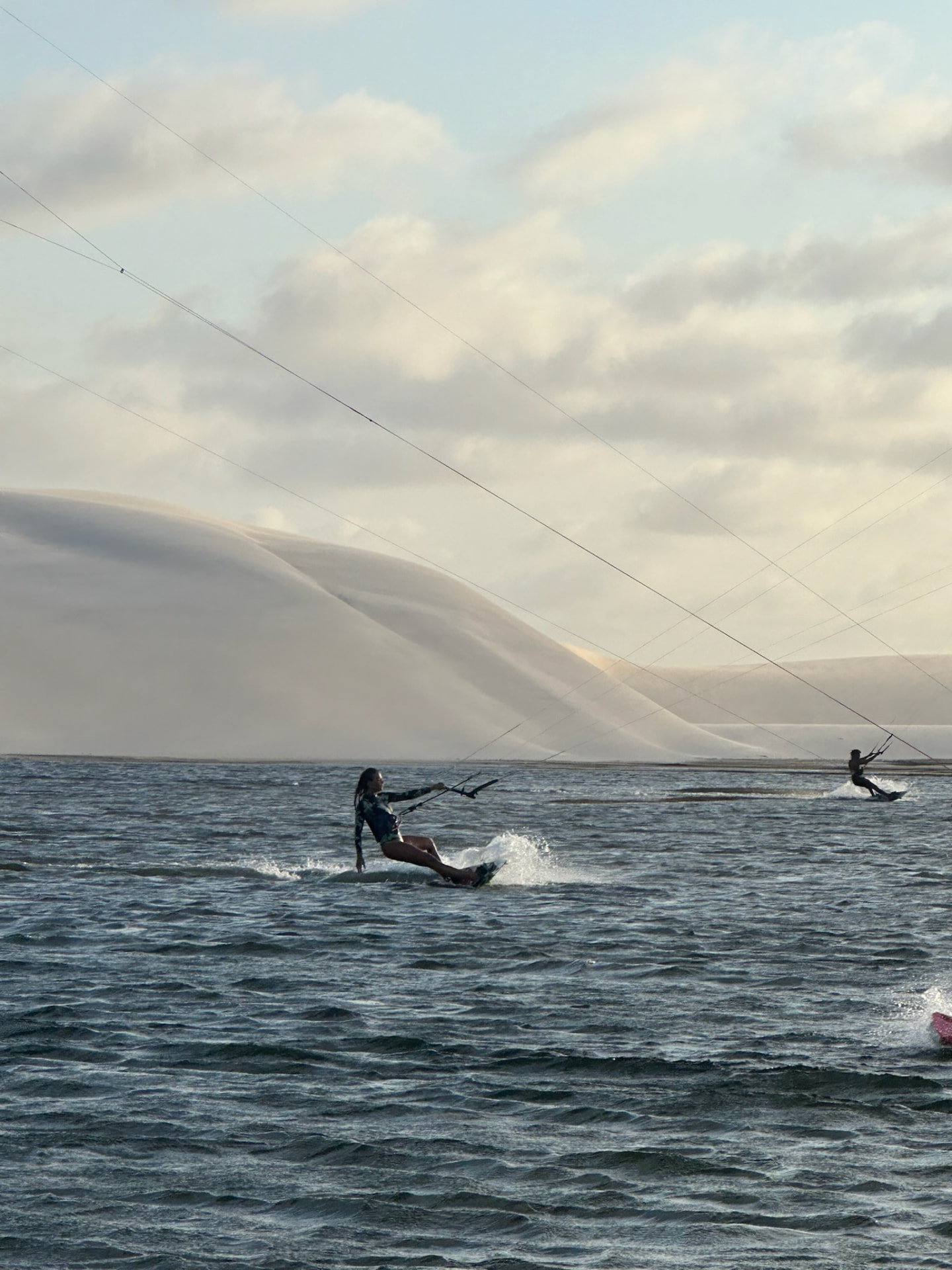 A kitesurfer riding in front of towering sand dunes